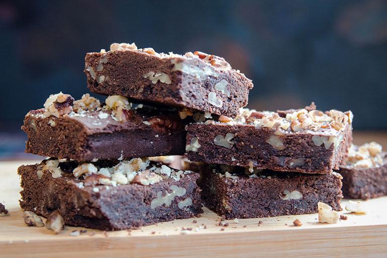 A stack of chocolate and pecan brownies, sprinkled with pecan crumbs and crushed walnut, fresh out of the oven