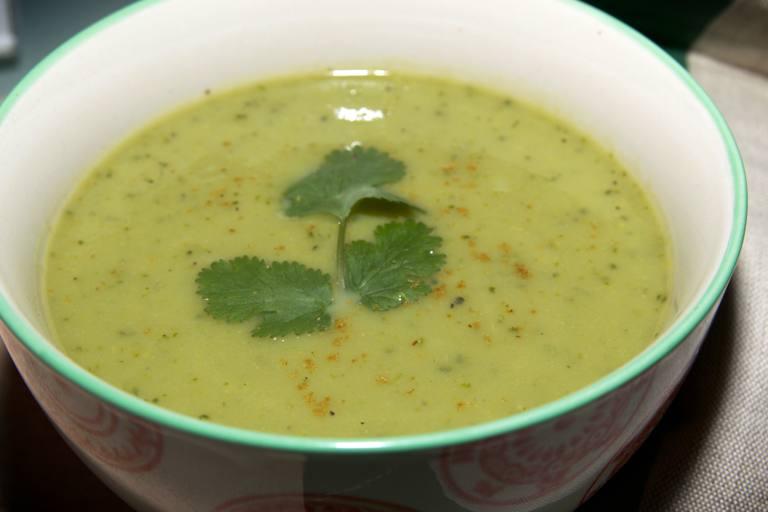 Watercress soup with a sprig of coriander as garnish in a white bowl with green trim.